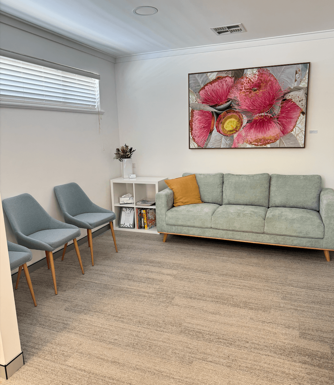 Our Rockingham waiting room, with a sage sofa, grey chairs, a bookshelf and a large pink gum blossom painting.